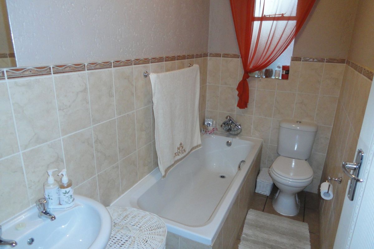 A functional bathroom featuring a built-in bathtub, pedestal washbasin, and close-coupled toilet with neutral ceramic wall and floor tiling.