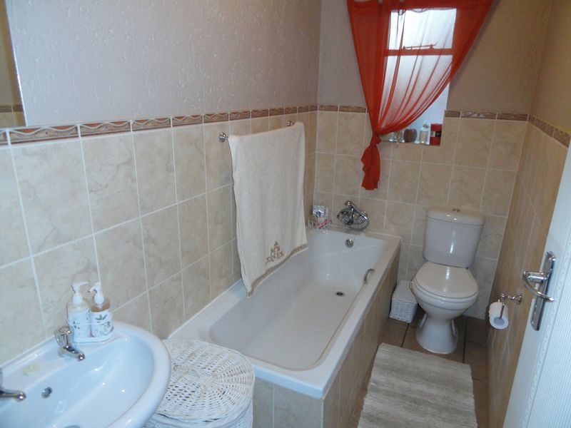 A functional bathroom featuring a built-in bathtub, pedestal washbasin, and close-coupled toilet with neutral ceramic wall and floor tiling.