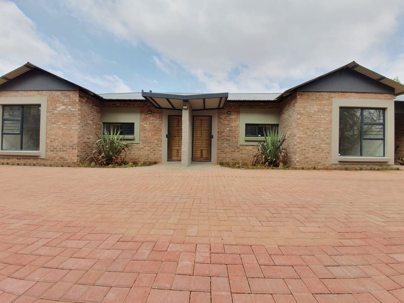 Front elevation of a modern townhouse featuring a face brick facade, paved driveway, and a covered entrance with timber doors.