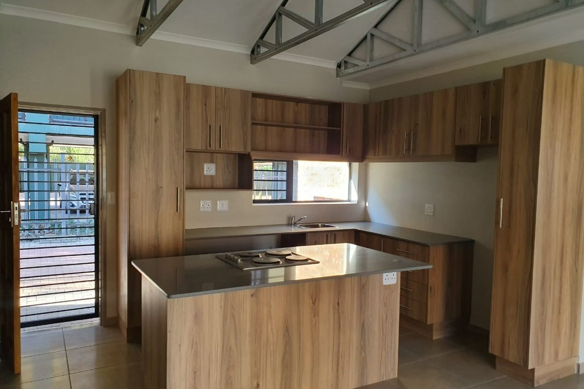 Modern kitchen featuring wood-finish cabinetry, a central island with a built-in hob, stainless steel sink, and exposed industrial-style roof trusses.