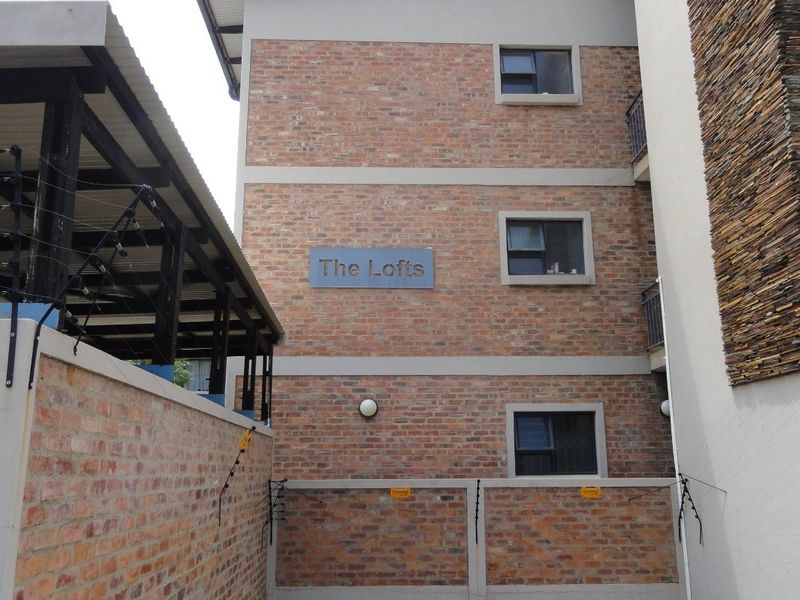 Exterior view of The Lofts apartment complex featuring face brick construction, stone cladding accents, and secure electric fencing.