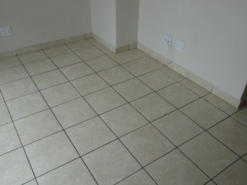 An empty room featuring neutral ceramic floor tiles, matching tiled skirting, and multiple electrical wall sockets.