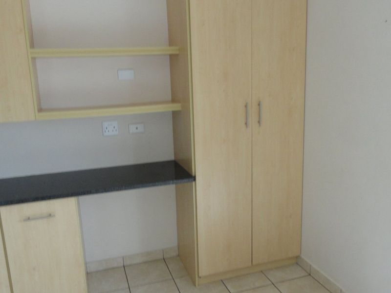 A bedroom featuring light wood built-in cupboards and a matching integrated desk with a dark countertop, set against neutral walls and tiled flooring.