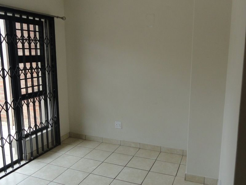 An empty living area featuring neutral tiled flooring and a secure sliding door leading to an outdoor space.