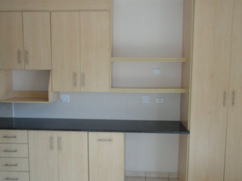 A functional kitchen featuring light wood-finish cabinetry, dark laminate countertops, built-in oven, and hob, offering a clean and practical workspace.
