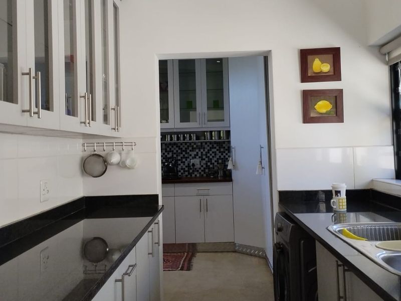 A well-maintained kitchen featuring granite countertops, white cabinetry, and a tiled backsplash, with an adjacent scullery area visible through the doorway.
