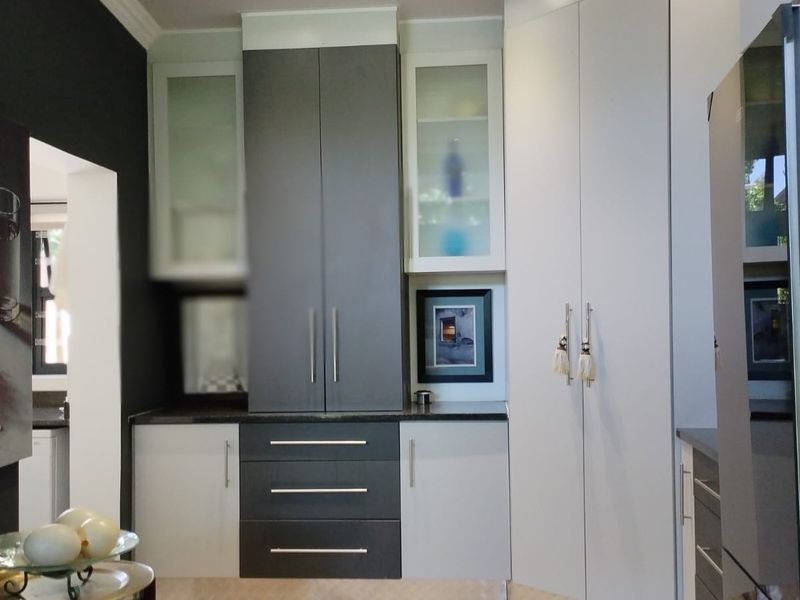 A modern kitchen featuring a mix of dark grey and white built-in cabinetry, granite countertops, and glass-fronted display units.