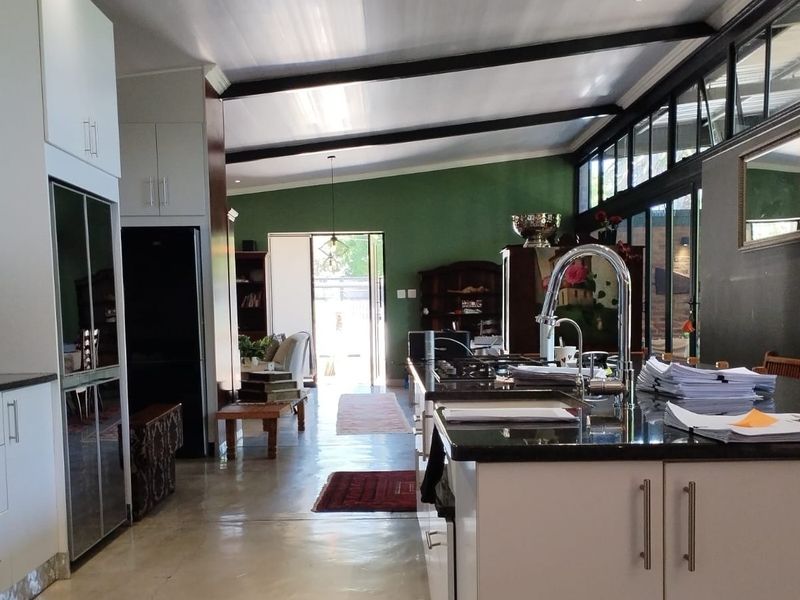 Spacious open-plan kitchen and living area featuring a large island, granite countertops, exposed ceiling beams, and expansive glass doors leading to the outdoors.
