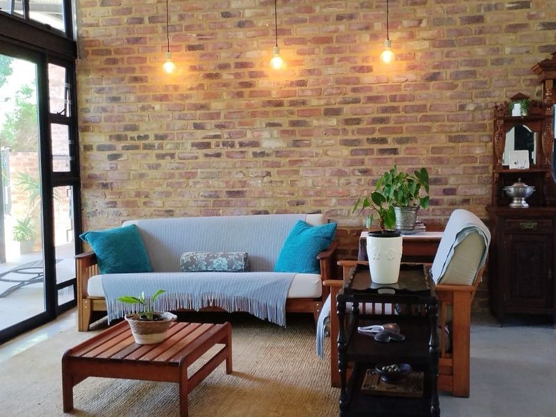 A bright living room featuring an exposed brick feature wall, polished concrete floors, and large black aluminium sliding doors leading to the outdoor area.
