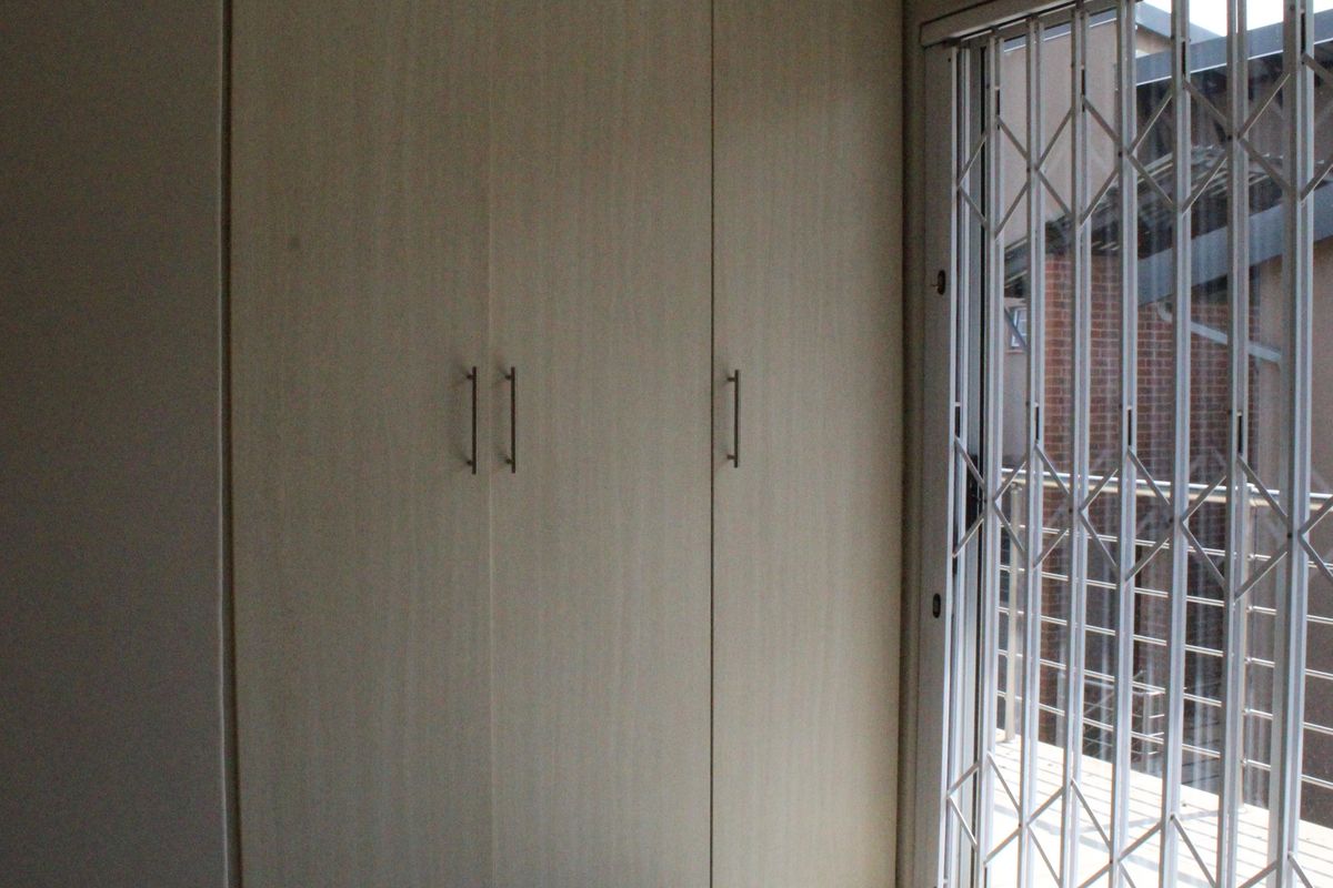 A bedroom featuring built-in wooden cupboards and a sliding door secured with a metal security gate, providing access to an outdoor area.
