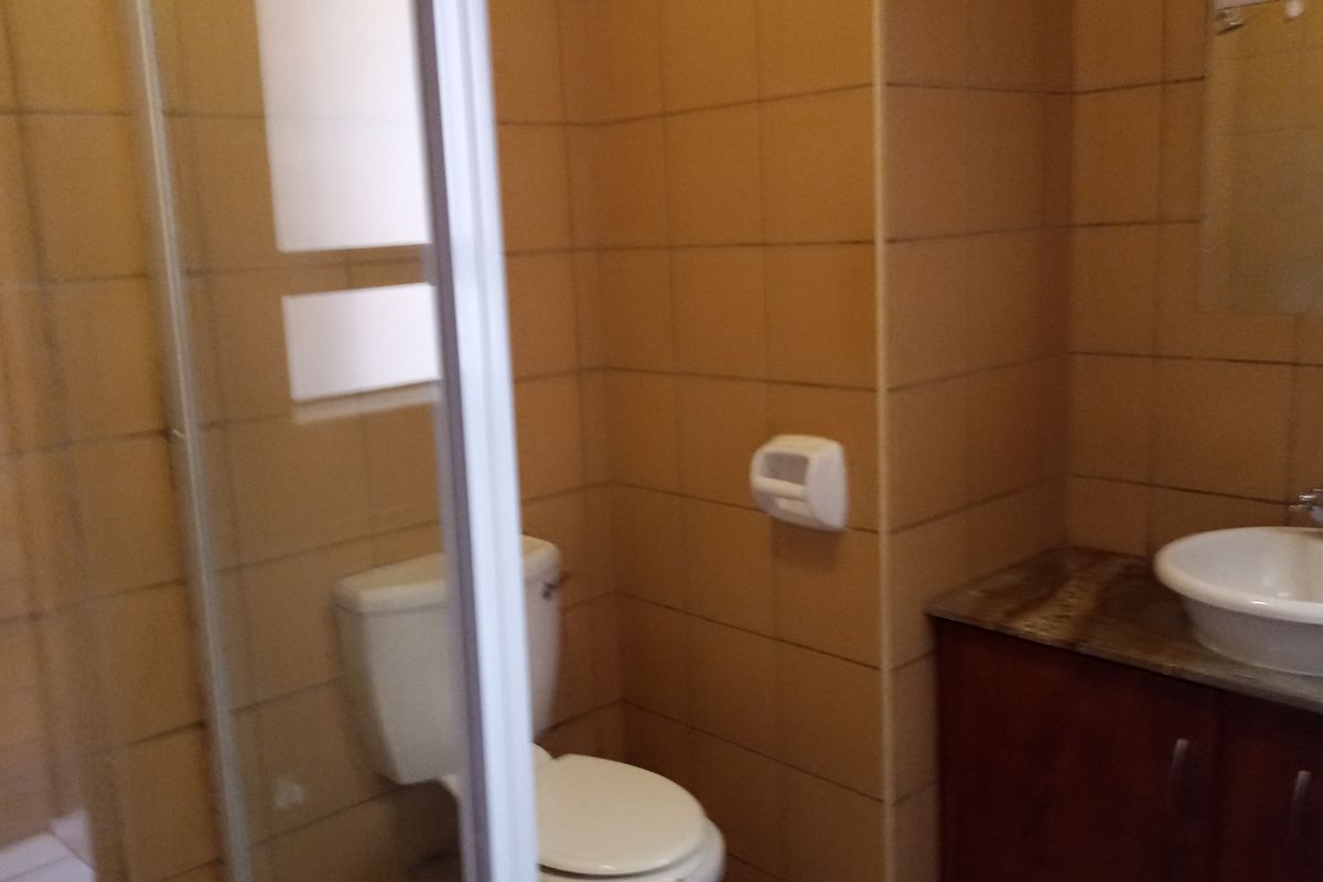 A functional bathroom featuring a glass-enclosed shower, a built-in vanity with a basin, and a toilet, finished with dated wall tiles.