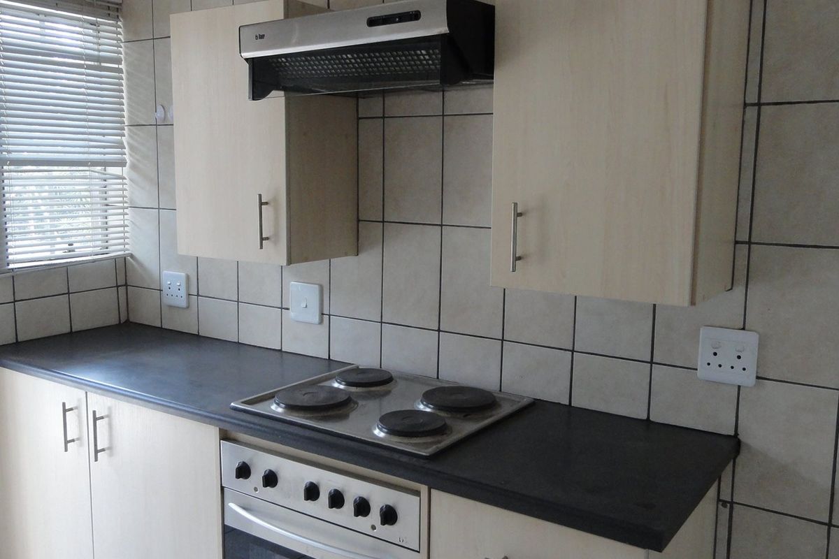 A functional kitchen featuring light-toned cabinetry, a dark laminate countertop, an integrated electric hob, oven, and extractor fan with tiled wall finishes.