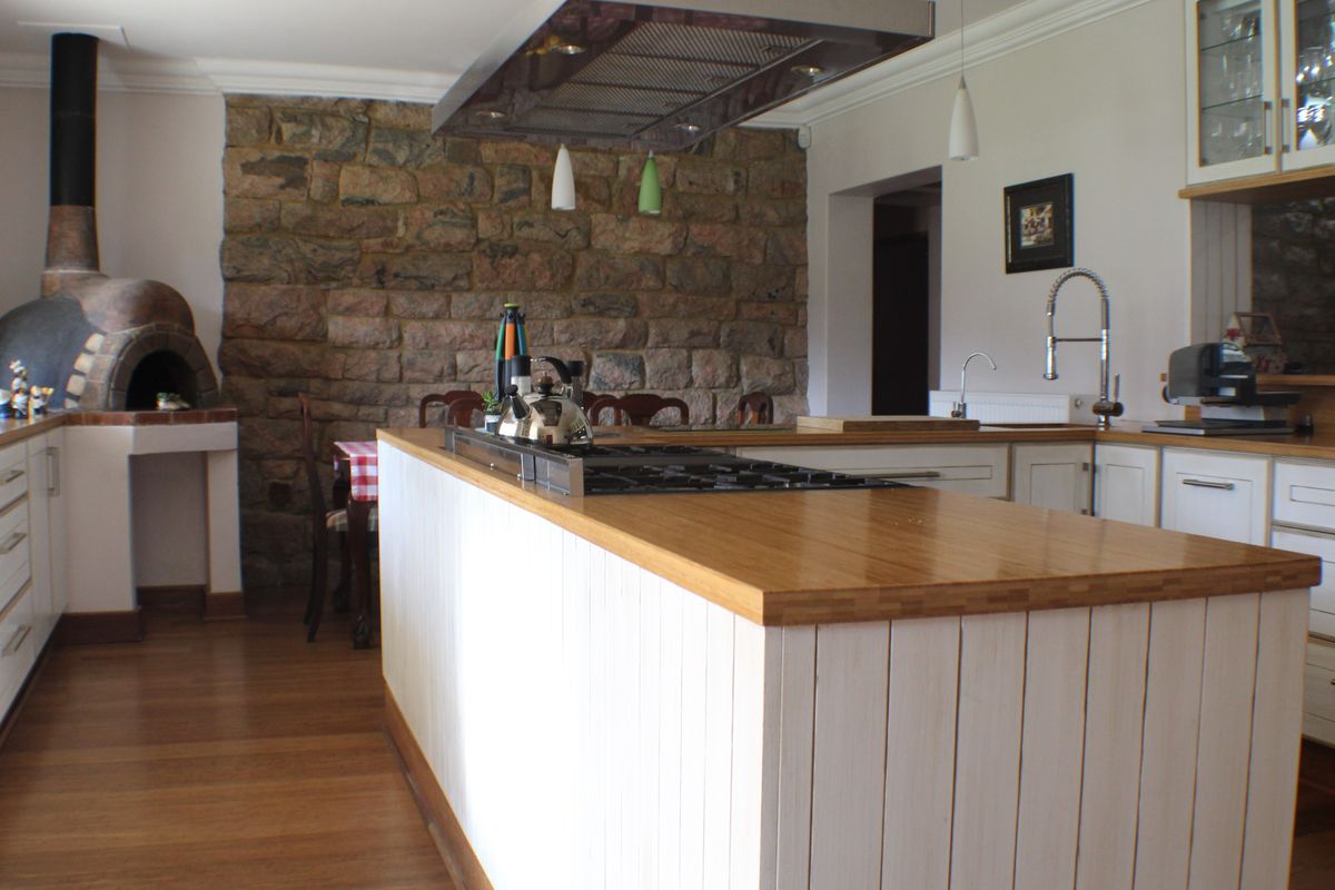 Spacious kitchen featuring a large central island with a gas hob, wooden countertops, and a built-in pizza oven set against a rustic stone feature wall.