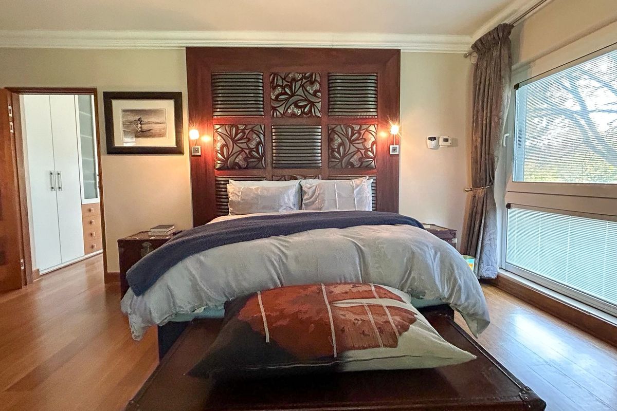 A well-maintained bedroom featuring hardwood flooring, a decorative built-in headboard with integrated lighting, and access to an adjoining walk-in closet.