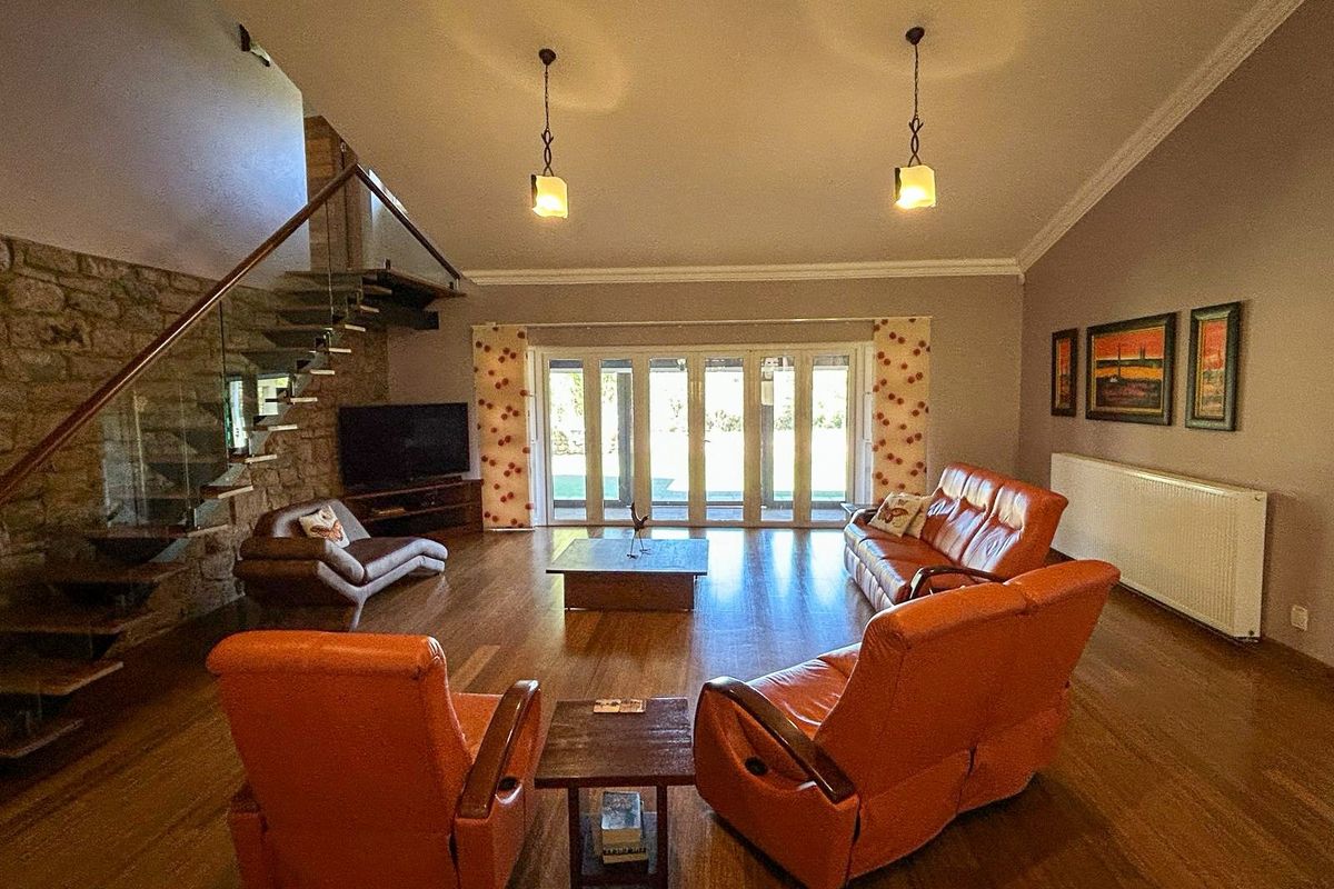 Spacious living room featuring high vaulted ceilings, hardwood flooring, a stone feature wall, and large glass folding doors leading to the garden.
