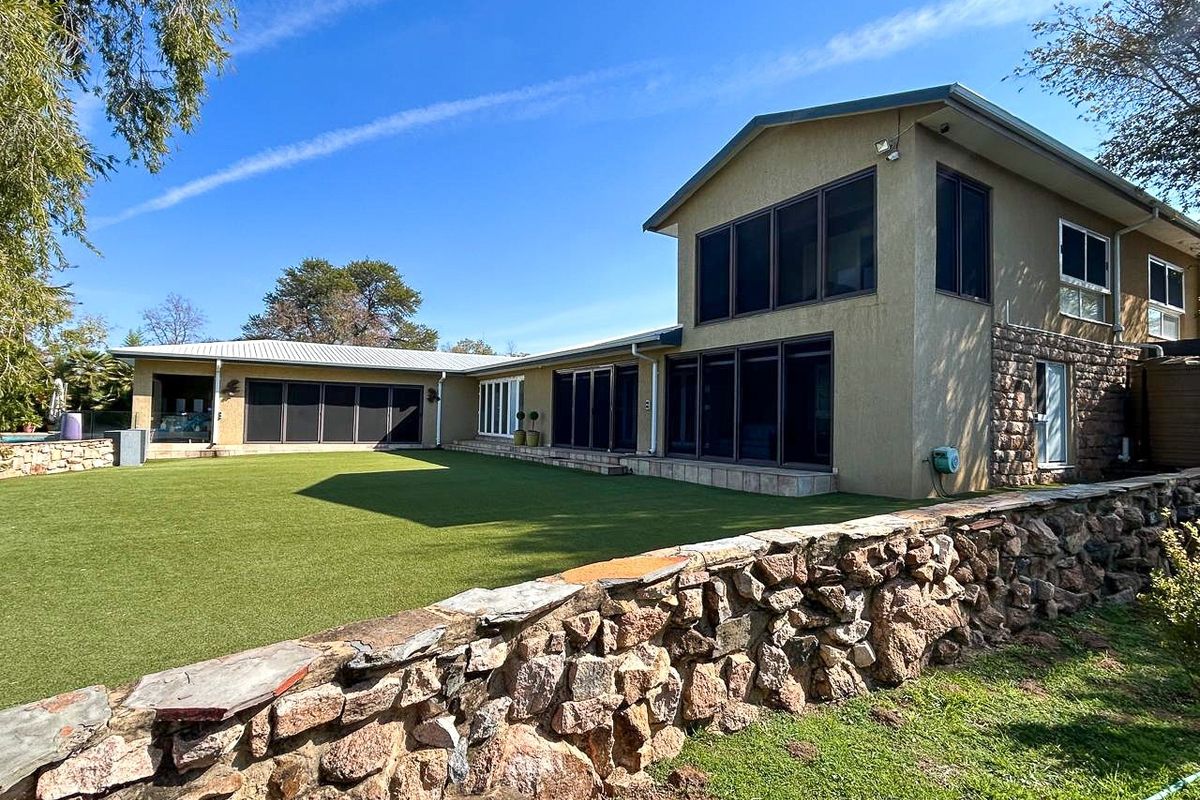 Spacious rear exterior view of the property featuring a large manicured lawn, stone boundary wall, and multi-level building structure with extensive glazing.