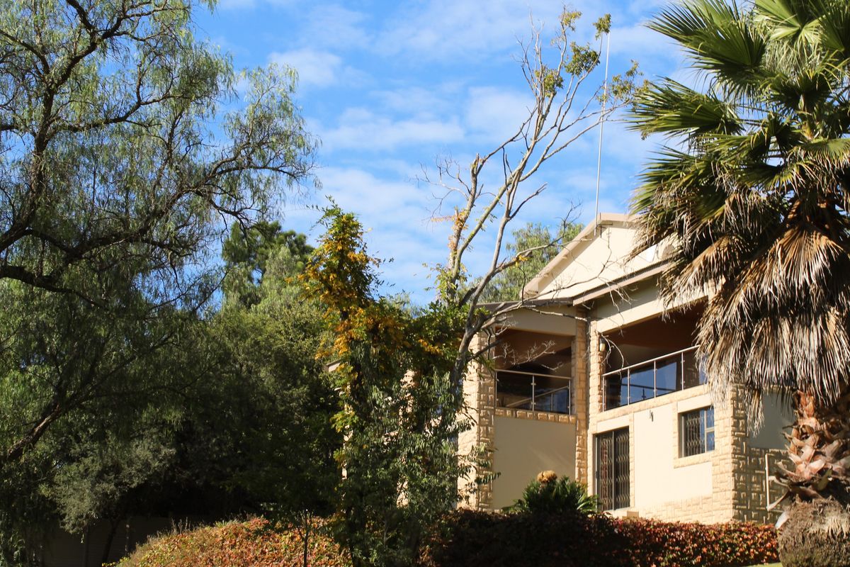 A view of the rear elevation of the property, featuring stone cladding, a covered balcony with glass balustrades, and established garden landscaping.