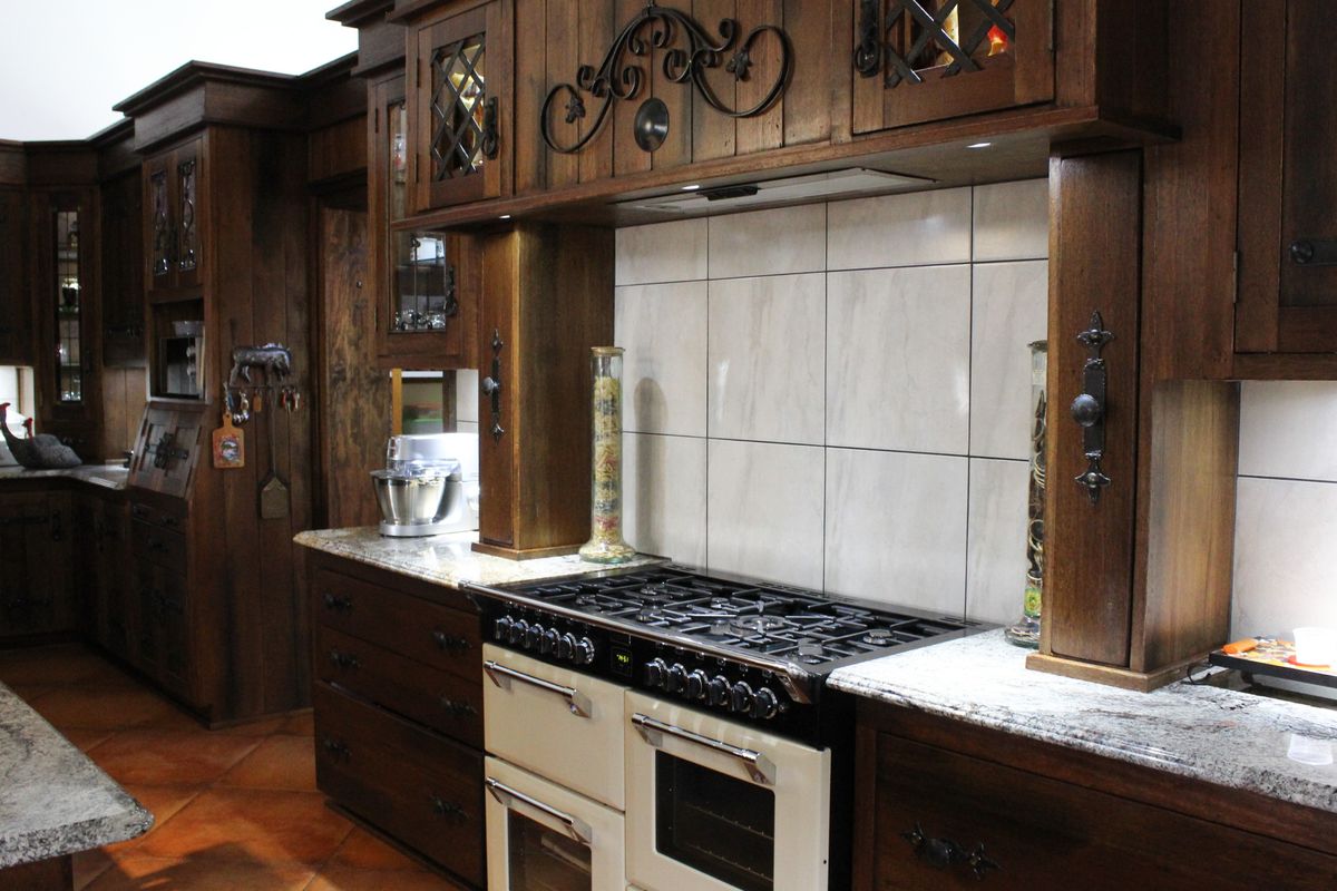 A traditional kitchen featuring dark wood cabinetry, granite countertops, a large dual-fuel range cooker, and tiled flooring.
