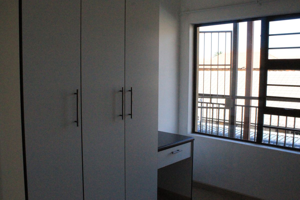 A bedroom featuring built-in cupboards with a integrated desk area and a window fitted with security bars.
