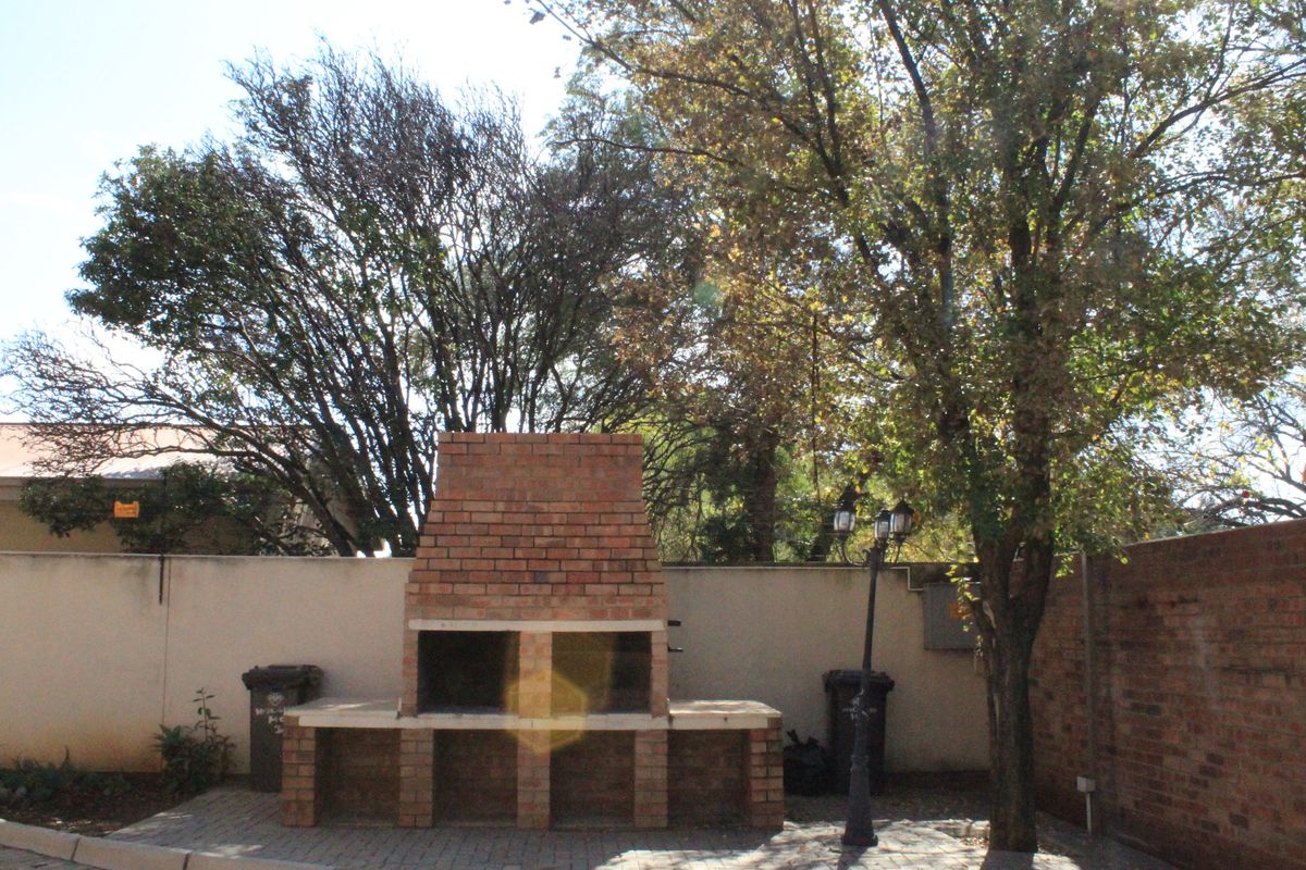 Outdoor area featuring a built-in brick braai or barbecue station set against a perimeter wall with mature trees.