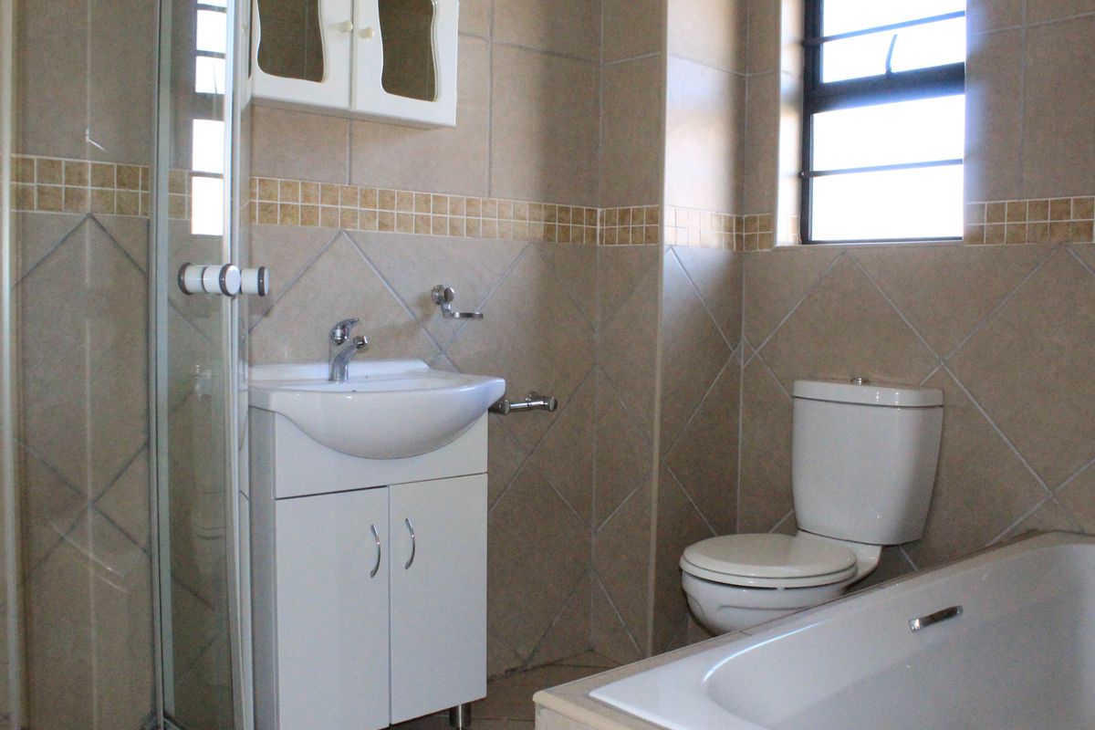 A functional bathroom featuring a shower enclosure, a vanity basin with storage, a toilet, and a bathtub with neutral wall tiling.