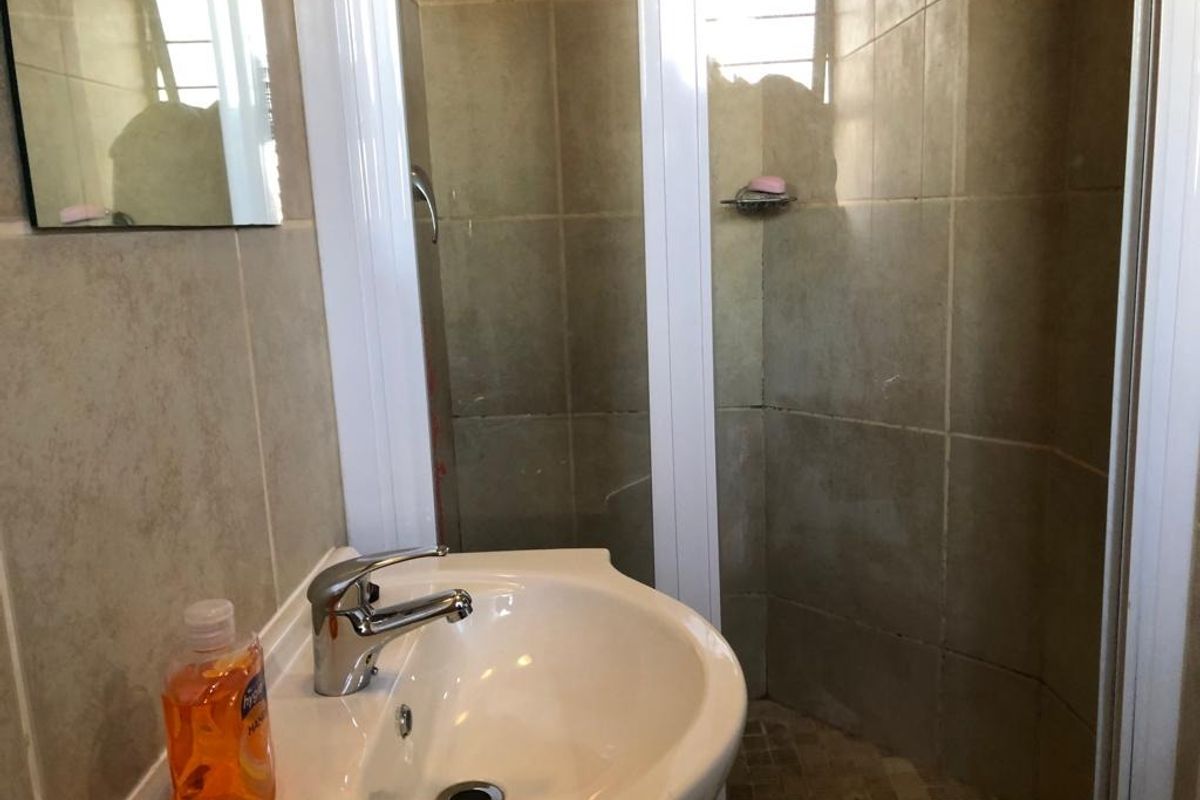 Compact bathroom featuring a corner shower enclosure with tiled walls and a pedestal basin with a chrome mixer tap.