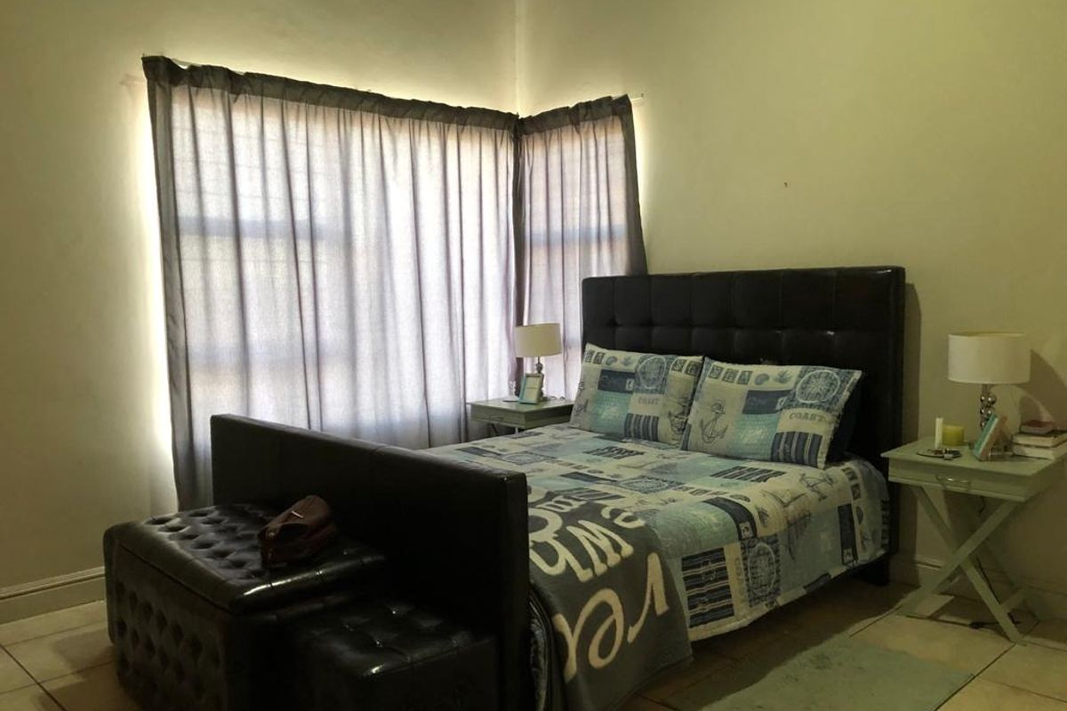 A bedroom featuring tiled flooring and large windows with curtains, providing a functional and comfortable living space.