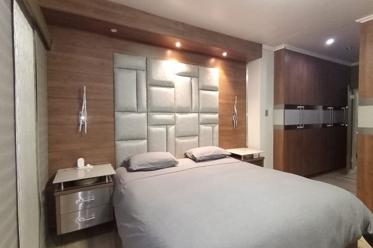 A well-appointed bedroom featuring custom built-in cabinetry, integrated headboard paneling with recessed lighting, and sleek modern finishes.