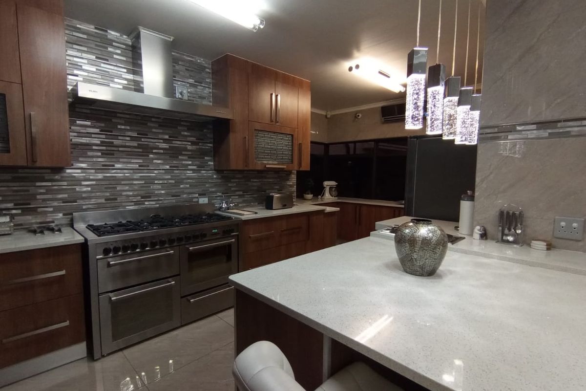 Modern kitchen featuring wood cabinetry, stone countertops, a large gas range with stainless steel extractor hood, and a central island with pendant lighting.