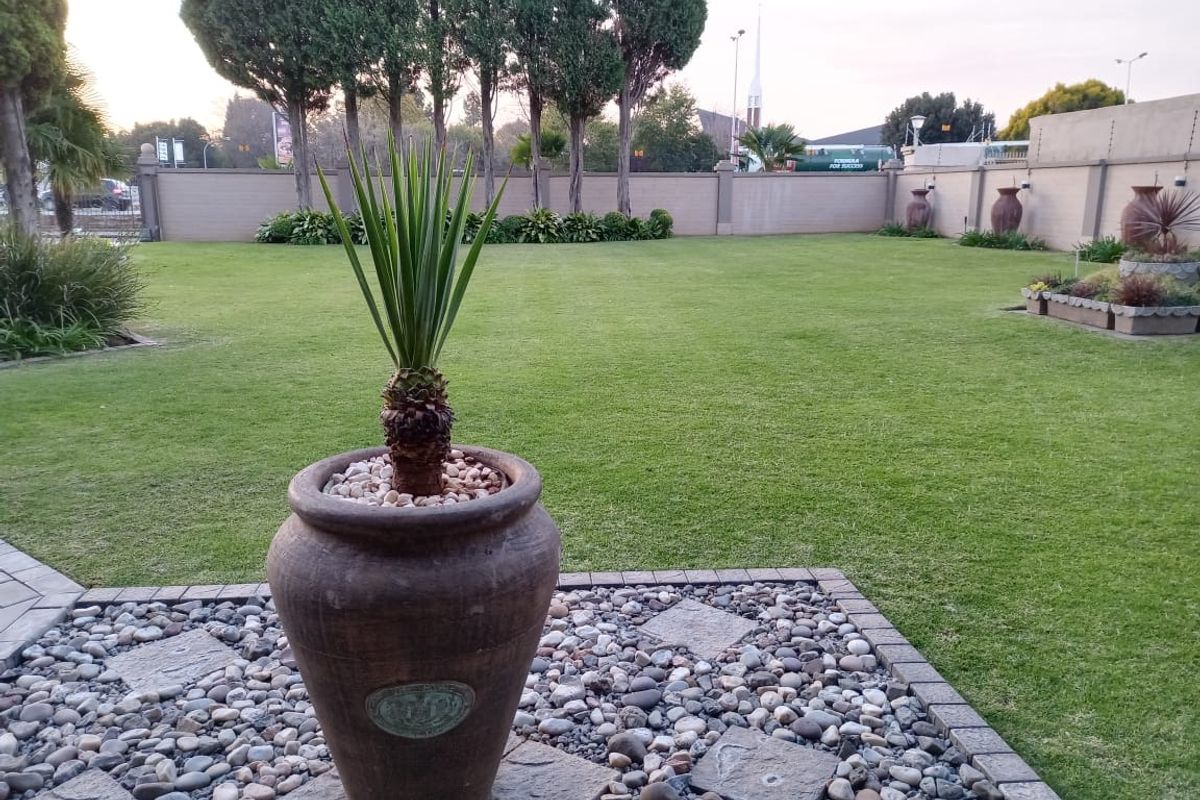 A well-maintained rear garden featuring a manicured lawn, perimeter boundary wall, and paved patio area with decorative stone landscaping.