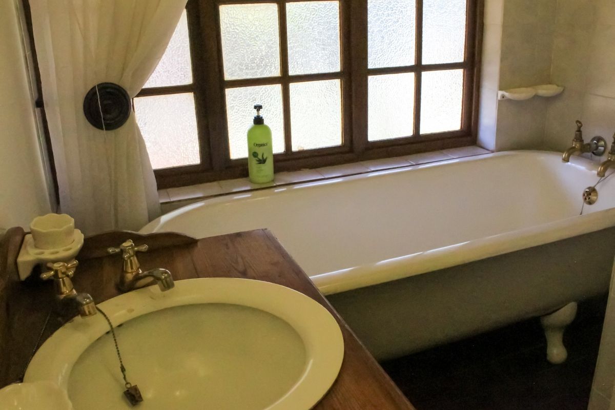 A classic bathroom featuring a clawfoot bathtub, timber vanity with integrated basin, and traditional brass-style tapware set against a multi-pane window.
