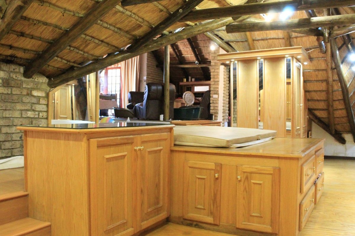 A unique loft-style bedroom featuring exposed timber beams, a thatched roof, and custom built-in wooden cabinetry with integrated storage.