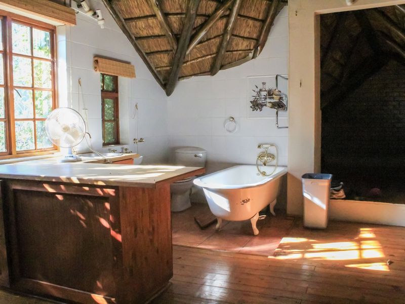 A rustic bathroom featuring a classic clawfoot bathtub, wooden vanity, and exposed thatch roof detailing, offering a unique and character-filled space.