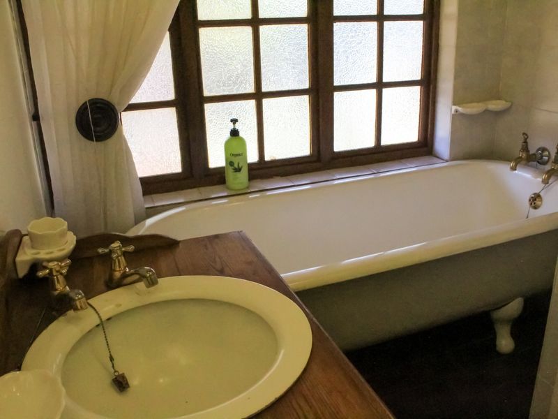 A classic bathroom featuring a clawfoot bathtub, timber vanity with integrated basin, and traditional brass-style tapware set against a multi-pane window.