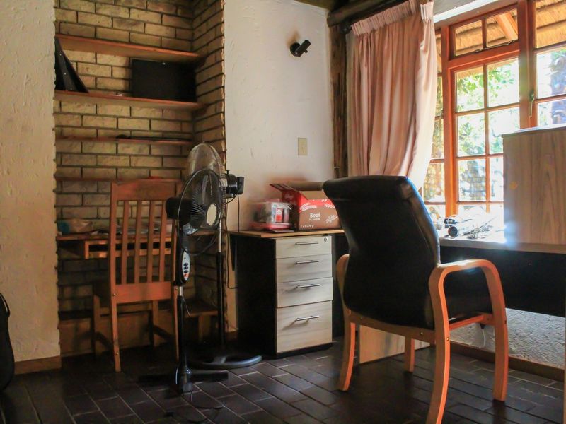 A home office space featuring exposed brick shelving, tiled flooring, and a timber-framed window providing natural light.
