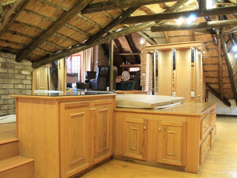 A unique loft-style bedroom featuring exposed timber beams, a thatched roof, and custom built-in wooden cabinetry with integrated storage.