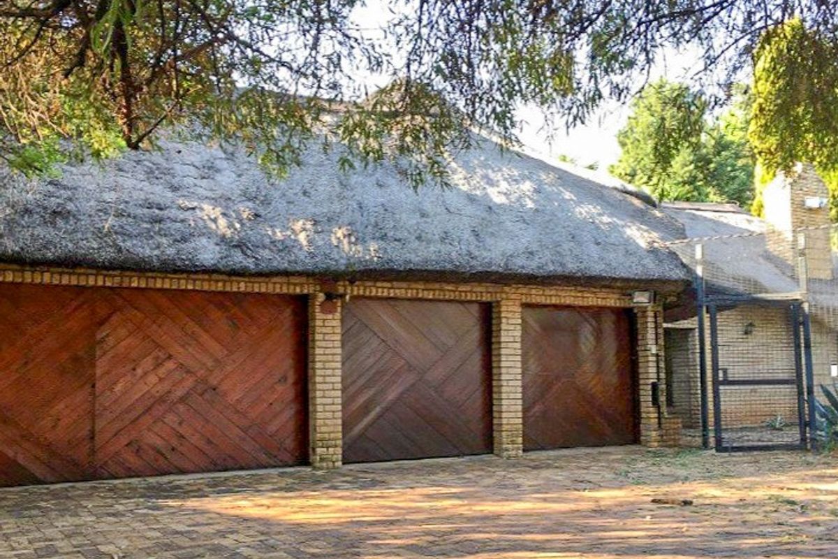 A triple garage featuring wooden doors and a traditional thatch roof, set against a paved driveway area.