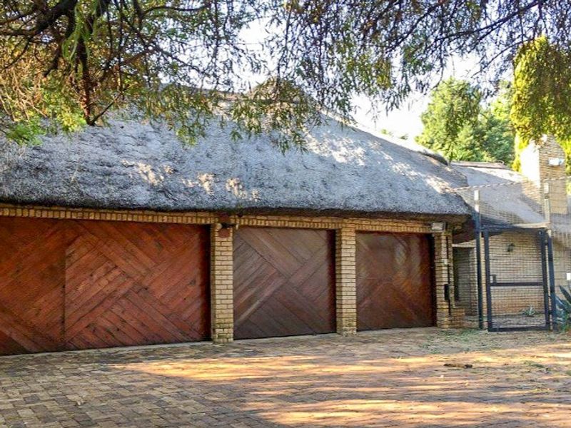 A triple garage featuring wooden doors and a traditional thatch roof, set against a paved driveway area.
