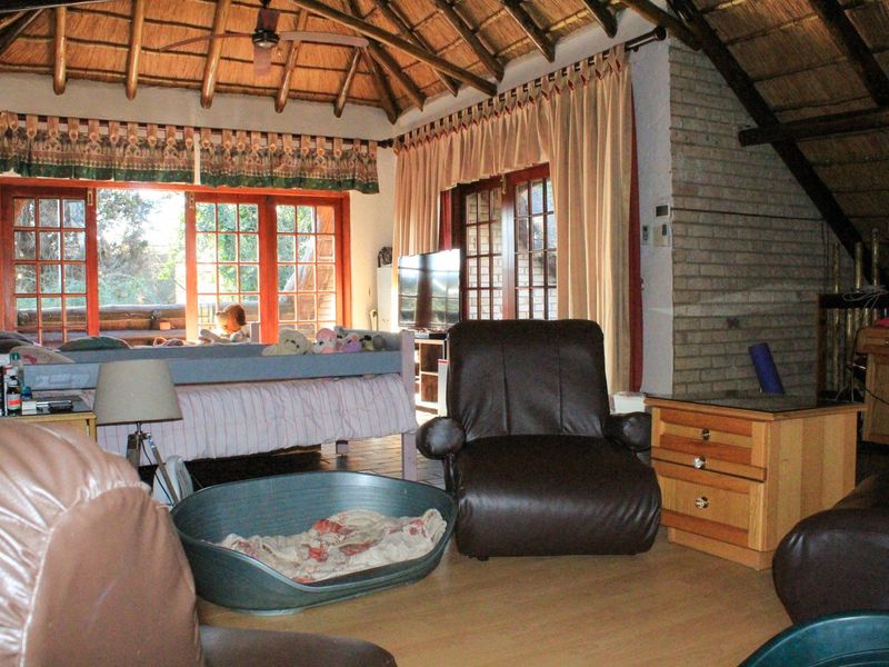 Spacious living area featuring a high vaulted thatched ceiling, exposed brickwork, and large wooden-framed glass doors providing access to the outdoor space.