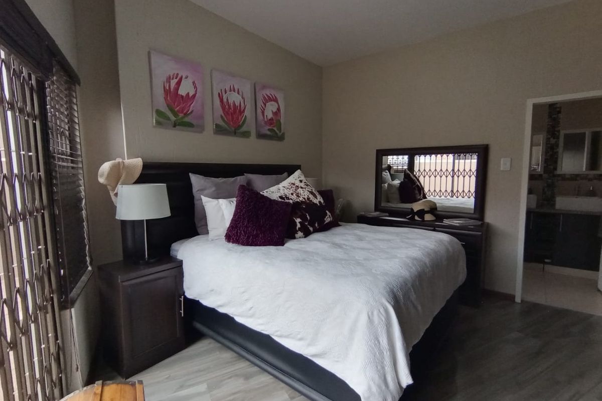 A well-maintained bedroom featuring wood-look laminate flooring, neutral wall tones, and direct access to an en-suite bathroom.