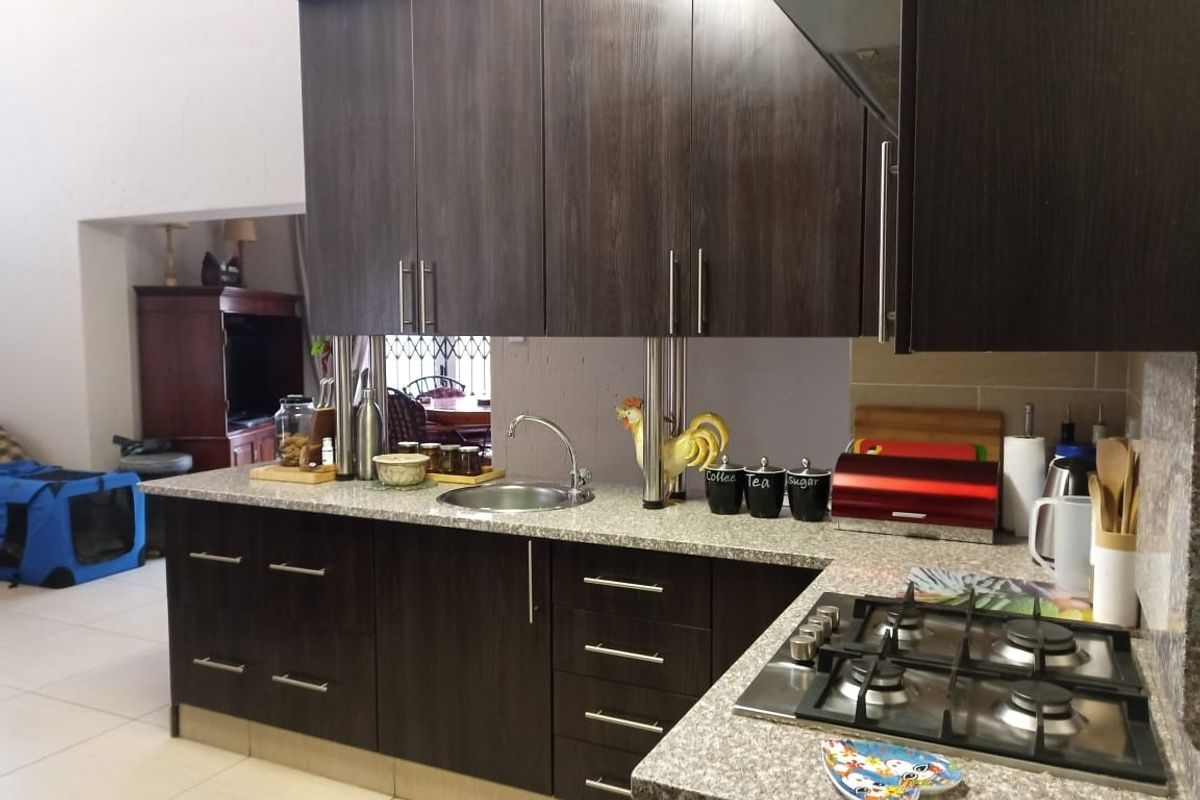 A functional kitchen featuring dark wood cabinetry, granite countertops, a built-in gas hob, and a stainless steel sink, with an open-plan layout.