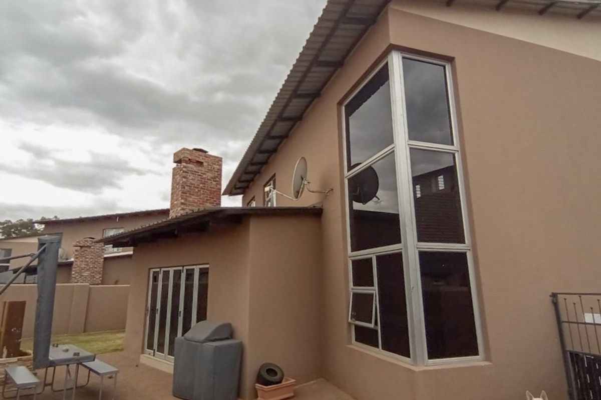 Rear exterior view of the townhouse featuring a paved patio area, brick chimney stack, and large double-height aluminium-framed windows.