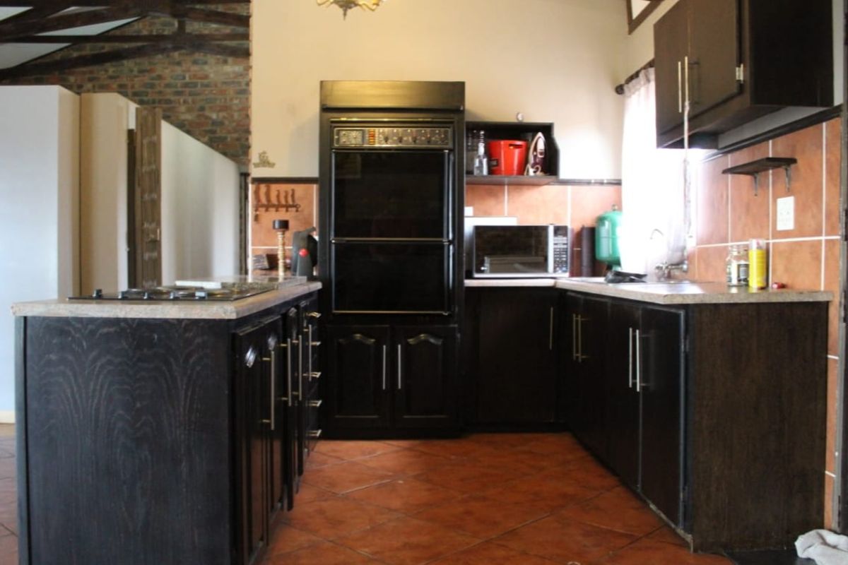A rustic kitchen featuring dark wood cabinetry, built-in double oven, gas hob, and exposed brickwork under a vaulted timber-beamed ceiling.