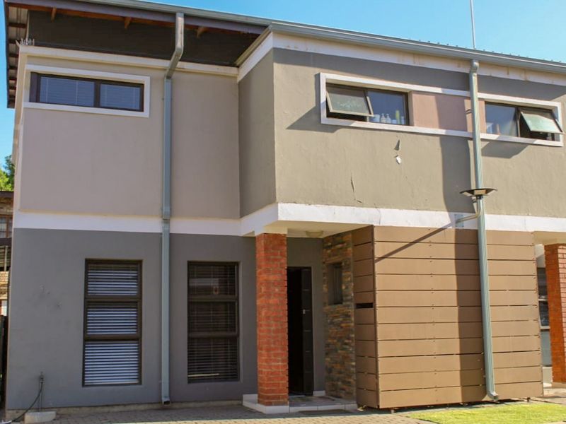 A modern two-story townhouse facade featuring a mix of painted plaster, brick columns, and horizontal cladding with aluminium window frames.