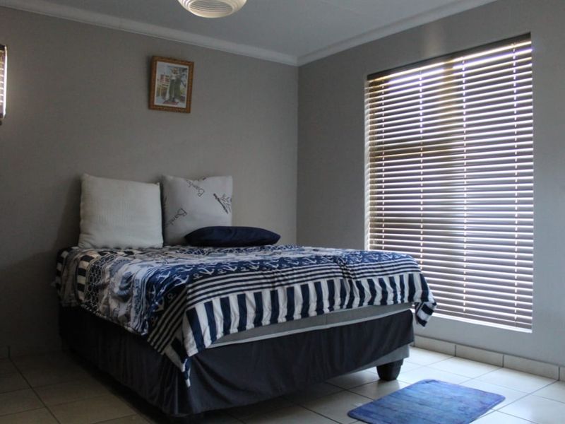 A bedroom featuring tiled flooring, neutral wall paint, and fitted window blinds, providing a functional and well-lit living space.