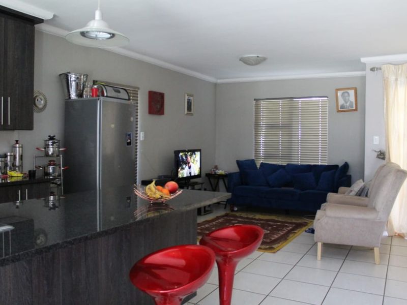 Open-plan living area featuring a modern kitchen with dark cabinetry, granite countertops, and tiled flooring, seamlessly flowing into a comfortable lounge space.
