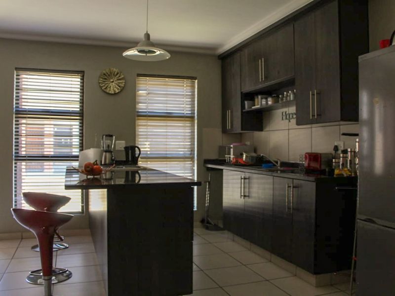Modern kitchen featuring dark wood cabinetry, granite countertops, a central breakfast island, and tiled flooring with natural light from large windows.