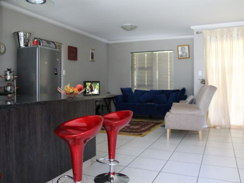 Open plan living area featuring a kitchen island with dark cabinetry and tiled flooring, seamlessly connecting to the lounge space.