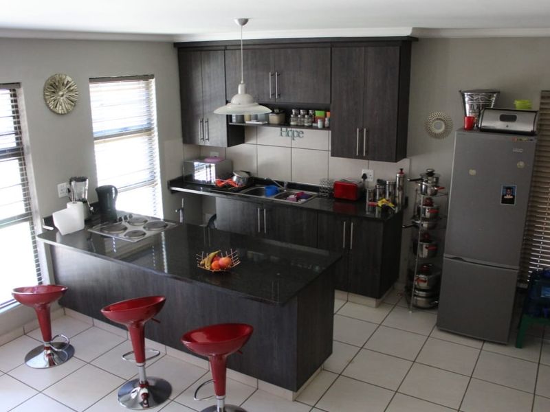 Modern kitchen featuring dark wood cabinetry, granite countertops, a breakfast bar, and tiled flooring with ample natural light.