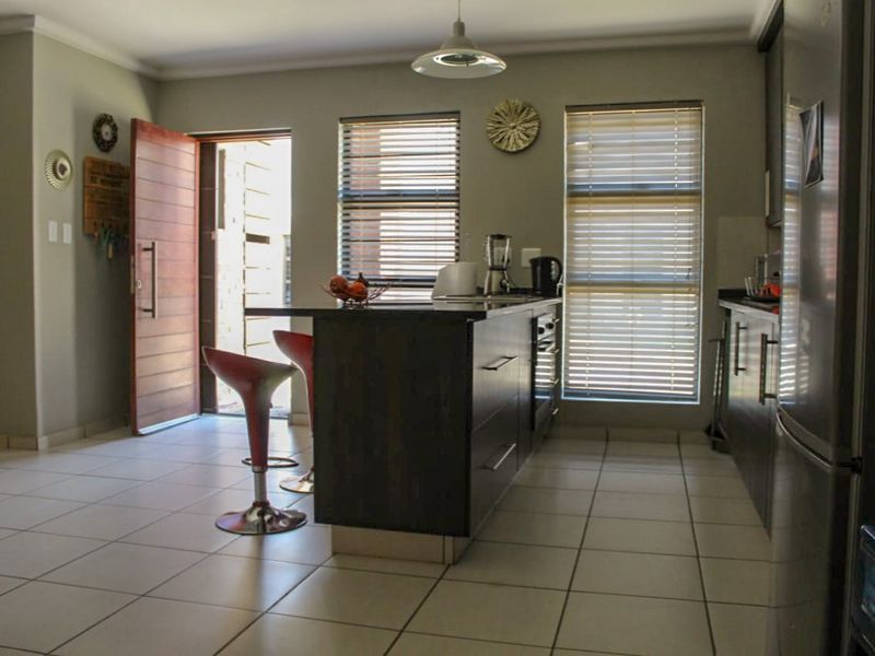 Modern kitchen featuring dark cabinetry, a central island with breakfast bar, tiled flooring, and direct access to the exterior.